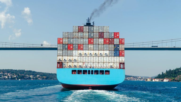 Parte trasera de un portacontenedores navegando bajo un puente